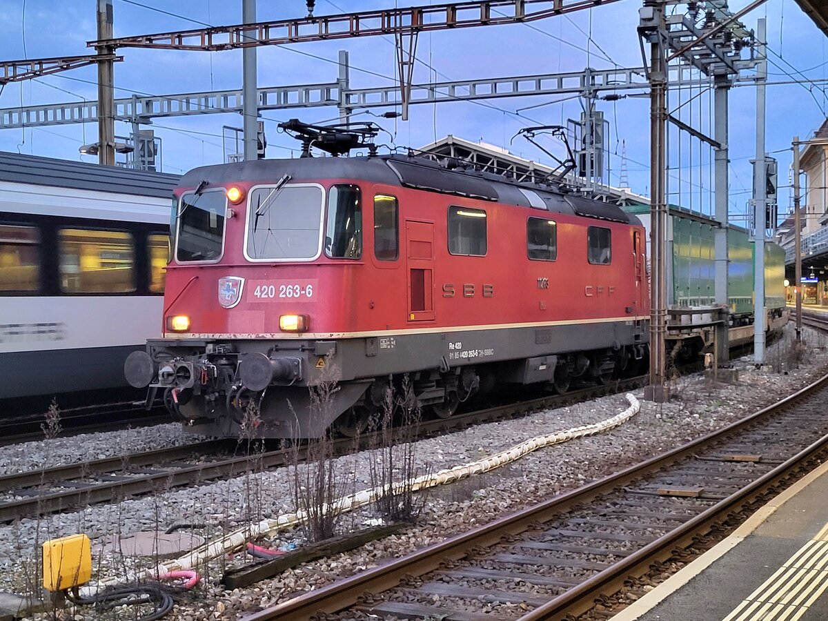 Die SBB Re 4/4 II 11263 (Re 420 263-6), welche mit einer automatischer Kupplung vom Typ Scharfenberg ausgestattet ist, wartet in Lausanne mit einem Güterzug, der ebenfalls über automatische Kupplungen verfügt, auf die Weiterfahrt nach St-Triphon. 

8. März 2025