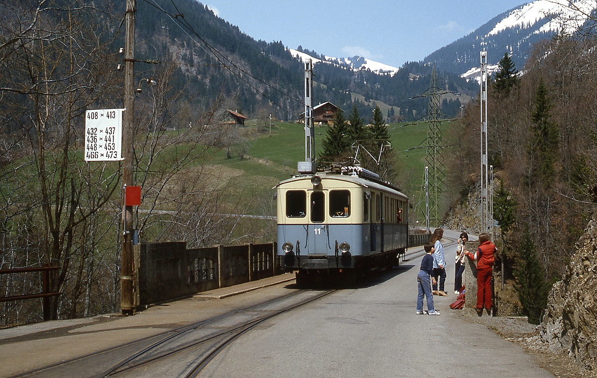 In Les Planches wartet ABFe 4/4 11 im Juli 1983 gemeinsam mit einigen Schulkindern auf den Gegenzug. Auf der links sichtbaren Tafel sind die Zugkreuzungen in Les Planches verzeichnet.