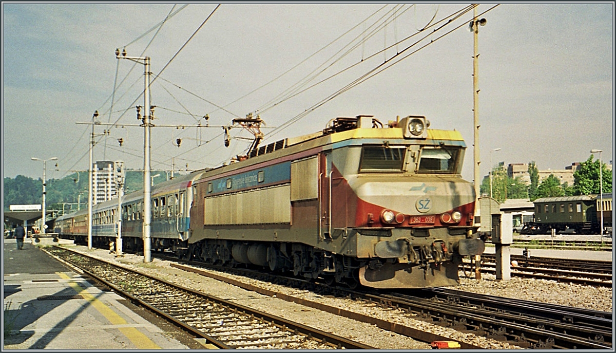 In Ljubljana steht die SZ 363 038 abfahrbereit mit einen Schnellzug in Richtung Beograd, an dritter Stelle nach den zwei SZ Wagen ist ein JZ Wagen zu erkennen. Die Lok ist in einer neuen, sehr gefälligen Farbgebung gehalten, welche an einigen SZ 363 die ursprüngliche JZ Farbgebung ablöste. 
Die eigenwillige Farbgebung setze sich aber nicht durch, wurde bei anderen Lokbaureihen nicht angewandt und später durch die  Karottenorange  Farbgebung abgelöst, die auch bei andern E-Lok Baureihen Anwendung fand, neuerdings (2023) soll jedoch eine hellblaue Farbgebung zu Norm werden. 

Analogbild vom Mai 2001