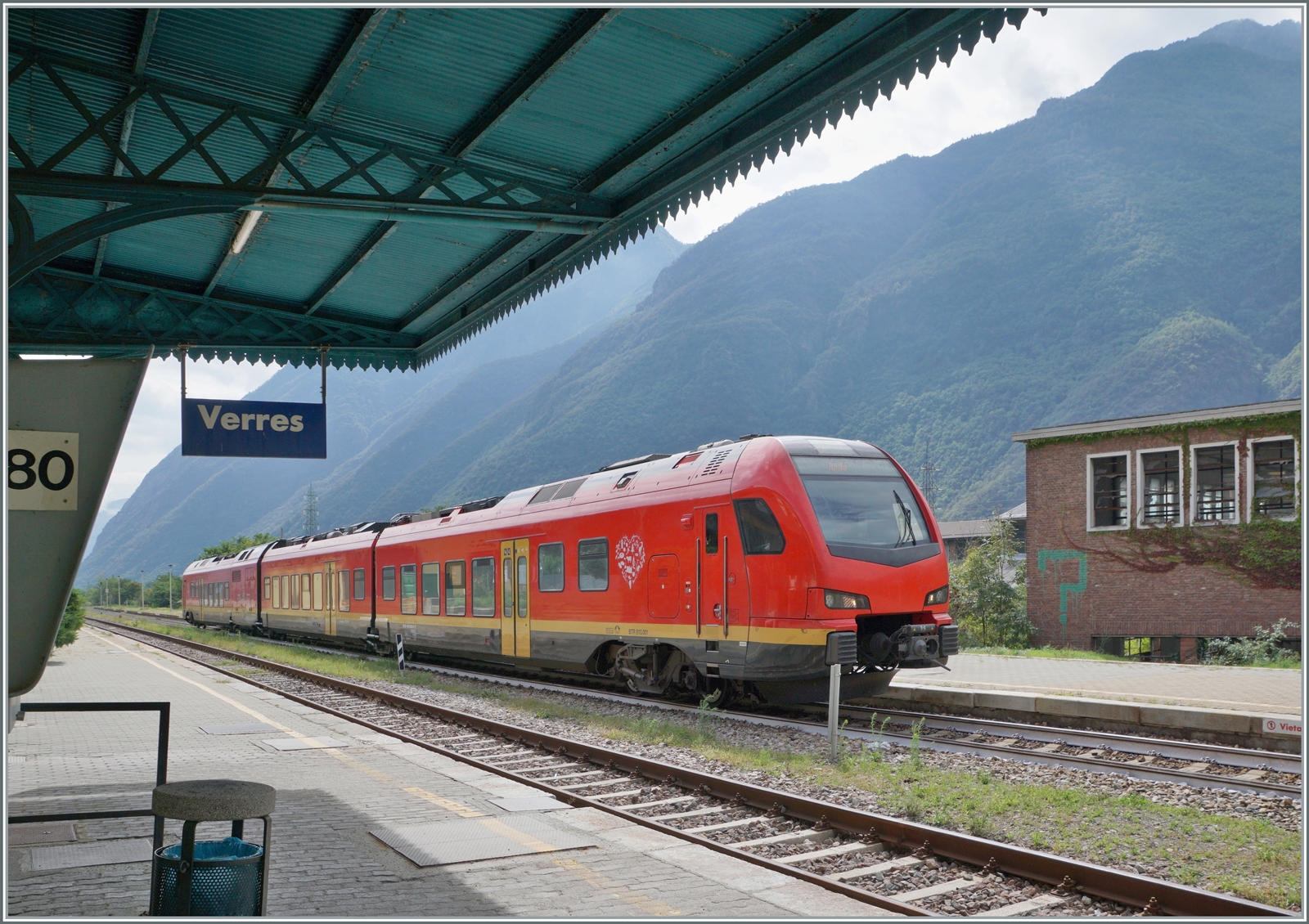 Der bimodulare FS Trenitalia BUM BTR 813 001 beim Halt in Verres im Aosta Tal. Der Zug ist als RE von Torino Porta Nuova nach Aosta unterwegs. Der Zug kann mit Dieselmotoren oder elektrisch mit 3000 Volt Gleichstrom betreiben werden, verfügt für die Achsanordnung Bo' 2'2'2' Bo'. Von Torino bis Ivrea nutzte der Triebzug die Fahrleitung, ab Ivrea seine Dieseltraktion. 

17. Sept. 2023