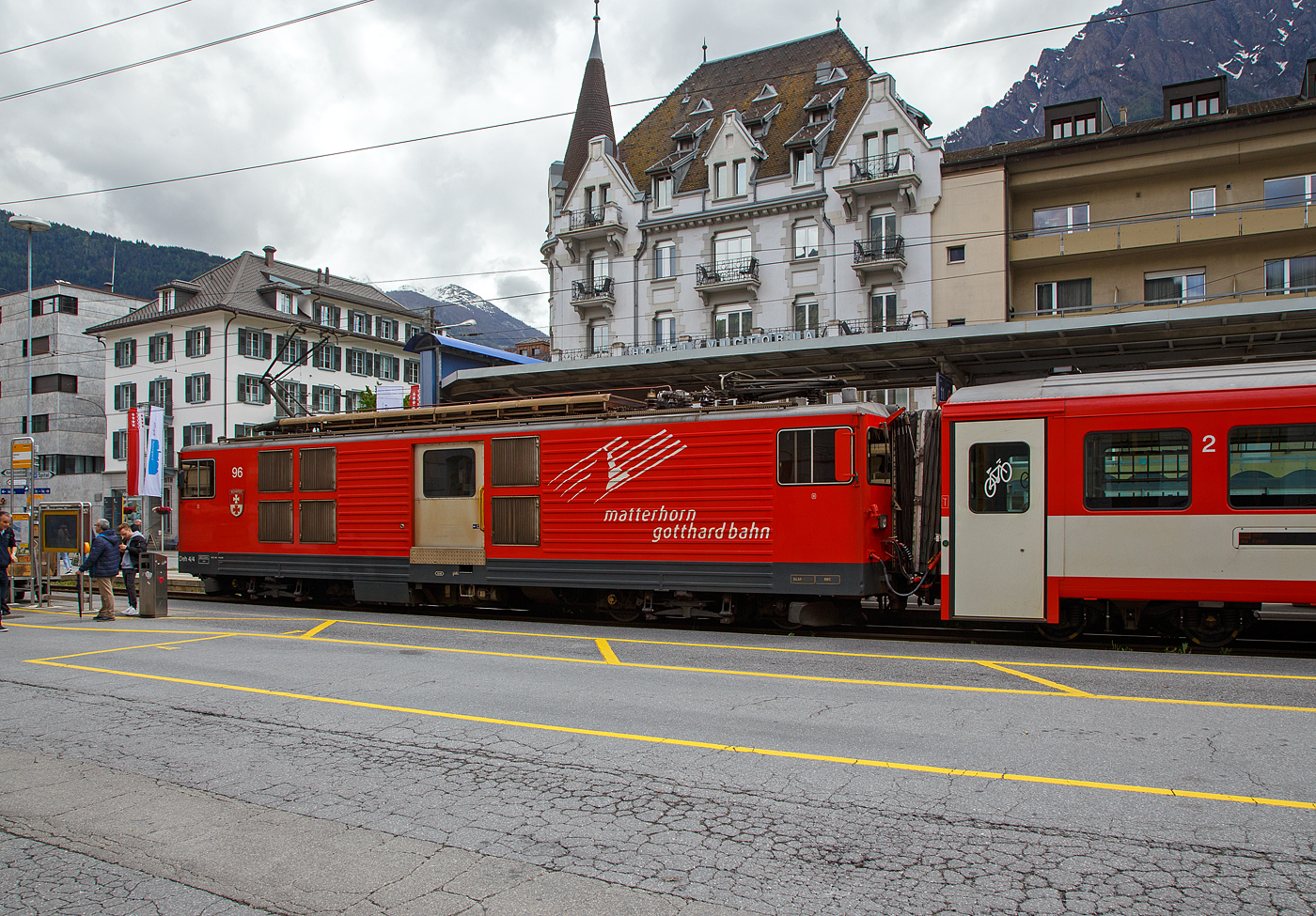 Der Gepäcktriebwagen Deh 4/4 II - 96  Münster   der Matterhorn-Gotthard-Bahn (MGB), ex FO 96  Münster   (Furka-Oberalp-Bahn), am 25.05.2023 mit einen Regionalzug von Andermatt nach Visp im Bahnhof (Vorplatz) Brig.

Der Elektrischer Zahnradtriebwagen wurde 1984 von SLM (mechanischer Teil, Lokomotivkasten) und BBC (elektrische Ausrüstung) gebaut.

Die vier 1980 bei der Furka- Oberalp-Bahn in Betrieb genommenen Gepäcktriebwagen sind für Adhäsions- und Zahnstangenstrecken konzipiert. Zwei weitere Einheiten wurden 1982 in Auftrag gegeben. Sie werden auf dem ganzen Streckennetz – maximale Steigung 179%o - als Triebfahrzeuge für Züge mit vier bis fünf Wagen eingesetzt. Der biege- und verwindungssteife, extrem leichte Kasten wurde in Stahl ausgeführt und die hohe Steifigkeit durch Strukturgebung erzielt. Dem leichten Innenausbau und der ergonomischen Führerstandgestaltung wurde ebenfalls besondere Aufmerksamkeit geschenkt.

Die Drehgestelle, die durch tiefliegende Drehzapfen über Traversen  mit dem Kasten verbunden sind, enthalten je zwei Antriebsmotoren. Die Betriebsverhältnisse erfordern drei unabhängige Bremssysteme.

Die ehemaligen Deh 4/4 I und II der FO (Furka-Oberalp-Bahn) werden im Einsatz nicht unterschieden, wenn nötig, dann anhand der Seriennummern 2.., 5.. und 9... Wobei sie sich optisch und technisch schon etwas unterscheiden. Sie werden hauptsächlich zusammen mit zwei Mittelwagen und einem Steuerwagen als fest gekuppelte Pendelzüge eingesetzt. Zwischen Disentis und Andermatt (Oberalp, 110‰) kann ein und zwischen Visp und Andermatt (Goms, 90‰) können zwei, im Sommer drei Verstärkungswagen angehängt werden. Zwischen Andermatt und Göschenen (Schöllenenschlucht, 179‰) sind keine Verstärkungswagen möglich. Die Pendelzüge sind innerhalb der Komposition mit der automatischen +GF+-Kupplung (GFN) verbunden. Für andere Verwendungen müssen die Kupplungen getauscht werden. Mindestens ein Triebwagen, früher waren dies meist Nr. 95 oder 96, dient als Ersatzfahrzeug für die übrigen Deh und wird auch allein für Überfuhren eingesetzt. Früher wurden auch Güterzüge nach Göschenen geführt.

TECHNISCHE DATEN:
Spurweite: 1.000 mm
Achsformel: Bo’Bo’
Länge über Puffer: 15.500 mm
Drehzapfenabstand: 8.800 mm
Achsabstand im Drehgestell: 2.790 mm
Größte Breite: 2.683 mm
Größte Höhe (bei abgesenkten Stromabnehmer): 3.880 mm
Leergewicht: 49,5 t (davon Mechanischer Teil 28 ,5 t)
Dienstgewicht: 51,0 t
Maximale Zuladung: 1,5 t
Gepäckraum Fläche: 10 m²
Höchstgeschwindigkeit: Adhäsion 60 km/h / Zahnstange 30 km/h
Stundenleistung: 1.032 kW
Dauerleistung: 936 kW
Stundenzugkraft am Rad: 117,2 kN
Dauerzugkraft am Rad: 101,2 kN
Maximale Zugkraft am Rad: 247,2 kN
Stromsystem: 11 kV 16,7 Hz AC
Anzahl der Fahrmotoren: 4