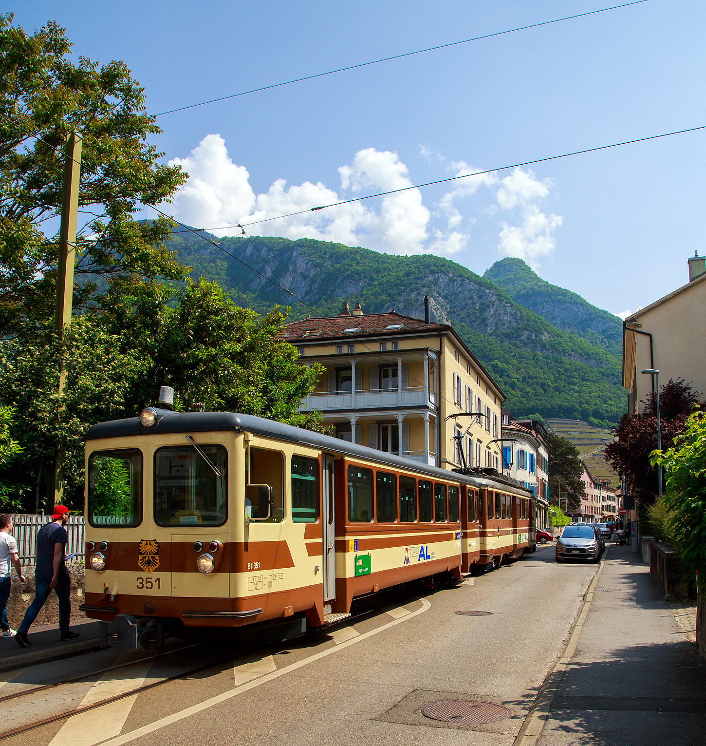Die Straßenbahn von Aigle kommt:
Der AL Regionalzug von Leysin nach Aigle fährt am 28. Mai 2023 (hier als Straßenbahn) durch Altstadt und erreicht bald den Bahnhof Aigle. Der Zug besteht aus dem führenden Steuerwagen AL Bt 351 „Aigle“  und dem Triebwagen AL BDeh 4/4 302 „Leysin“, beide sind noch im ursprünglichen Anstrich der AL (es sind auch die einzigen). 

In Aigle (Waadt) gibt es gleich drei Schmalspurbahnen, die seit 1999 in die Transports Publics du Chablais (TPC) fusioniert worden sind, so machten wir auf unserer Rückreise hier mal einen kurzen Zwischenhalt. Die Schmalspurbahnen sind die Aigle–Ollon–Monthey–Champéry-Bahn (AOMC), die Aigle–Sépey–Diablerets-Bahn (ASD), seit dem 22. Dezember 1913 und die Aigle–Leysin-Bahn (AL).

Die Chemin de fer Aigle–Leysin (AL), deutsch Aigle-Leysin-Bahn, war eine Eisenbahngesellschaft im Schweizer Kanton Waadt. Ihre von 1900 bis 1916 eröffnete 6,2 Kilometer lange Strecke führt von Aigle im Rhonetal hinauf nach Leysin-Grand Hôtel. Die gemischte Zahnradbahn in der Spurweite 1.000 mm (Meterspur) mit dem System Abt wird seit der Betriebsaufnahme elektrisch betrieben. Im Jahr 1999 fusionierte die AL zu den Transports Publics du Chablais (TPC).

Die Bahnstrecke Aigle–Leysin hat ihren Ausgangspunkt vor dem SBB-Bahnhof und führt als Straßenbahn auf der Rue de la Gare (Bahnhofstraße), der Avenue des Ormonts und über die Grande Eau zum Kopfbahnhof Aigle-Dépôt. Dort ändern die Züge die Fahrtrichtung, damit das Triebfahrzeug für die anschließende Bergfahrt am Ende des Zuges eingereiht ist. 

Im Keilbahnhof Aigle-Dépôt beginnt der 5,3 Kilometer lange und bis zu 230 Promille steile Zahnstangenabschnitt. Zunächst führt er durch die Rebberge und bietet den Fahrgästen einen Ausblick auf das Rhonetal. Bei der Haltestelle Pont-de-Drapel wechselt die Vegetation und das Trassee befindet sich nun im Wald. Der Zug erreicht eine Waldlichtung mit dem Bahnhof Rennaz (Leysin), wo er sich in der Regel mit dem Gegenzug kreuzt. Die Strecke führt weiter durch Wald und den 154 Meter langen Tunnel Rennaz. Ab rund 1.200 Meter über Meer fährt die Zahnradbahn durch Weiden und erreicht nach kurzer Zeit den Bahnhof Leysin-Village (Leysin-Dorf). Hier beginnt der Doppelspurabschnitt mit der 128 Meter langen Brücke Leysin nach Leysin-Feydey. Nach dem 287 Meter langen Kehrtunnel Leysin erreicht die Strecke, immer noch mit Zahnstange versehen, den Endpunkt Leysin-Grand Hôtel.


Die Triebwagen und Steuerwagen BDeh 4/4 301–302 und Bt 351–352 wurden 1966 von SIG/SAAS gebaut. 

TECHNISCHE DATEN:
Spurweite: 1.000 mm
Fahrleitungsspannung: 1.500 V =

Triebwagen: BDeh 4/4 301-302
Zahnstangensystem: Abt
Achsfolge: Bo'zz Bo'zz
Länge über Puffer: 16.100 mm
Drehzapfenanstand: 9.540 mm
Achsabstand im Drehgestell: 2.460 mm
Leistung: 596 kW (808 PS)
Treibraddurchmesser: 840 mm (neu)
Zahnrad-Teilkreisdurchmesser: 650
Höchstgeschwindigkeit: 40 km/h
Übersetzung: 1:12,2
Gewicht: 33.0 t
Sitzplätze: 48
Max. Ladegewicht: 1,5 t

Steuerwagen Bt 351–352
Anzahl der Achsen: 4
Gewicht: 11.0 t
Sitzplätze: 48