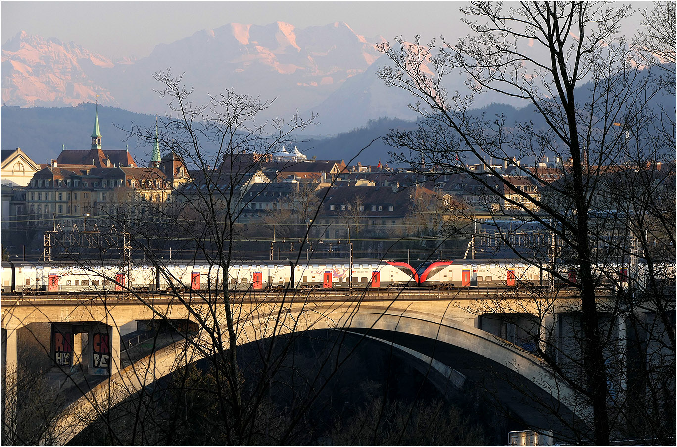 Mit Peter unterwegs in Bern - 

Bei schon tief stehender Abendsonne fährt eine RABe 502 Doppeltraktion über den Lorraineviadukt kurz vor dem Hauptbahnhof Bern.

Die Berggipfel: Ganz links das Gspaltenhorn, in Bildmitte zusammenhängend der Morgenstern, Wyssi Frau und Blüemlisalphorn, dann hinter dem Zweig der Niesen und hinter dem Baumstamm das Doldenhorn.

07.03.2025 (M)
