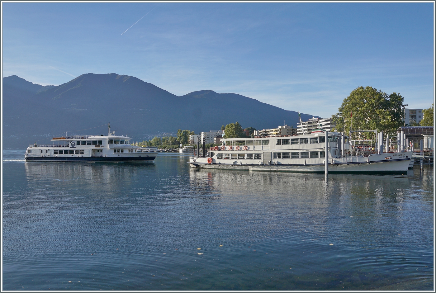 Während das Motoschiff  MILANO  im bei der Schiffanlegestelle von Locarno steht, nähert sich im Hintergrund ein weiteres Ausflugsschiff der Navigazione Lago Maggiore (NLM). 

17. Sept. 2025